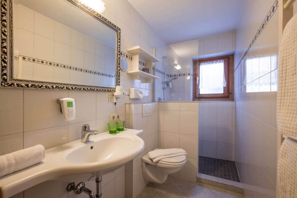 Modernes helles Badezimmer im Hotel Penzinghof mit Dusche, Waschbecken und Fenster.