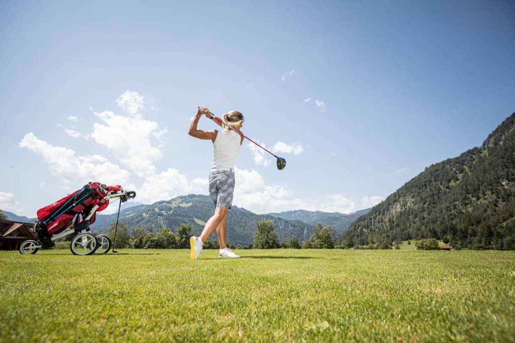 Golfer teeing off on a course in the middle of the Tyrolean alpine landscape.
