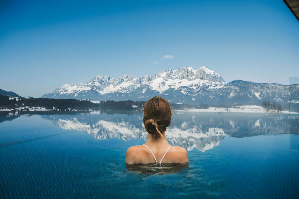 Femme dans la piscine à débordement avec vue sur les montagnes enneigées