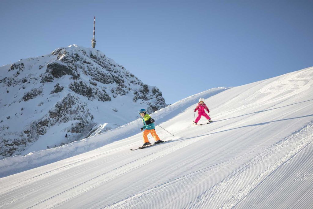 Enfants faisant du ski dans les Alpes tyroliennes avec des pistes enneigées et des sommets montagneux.