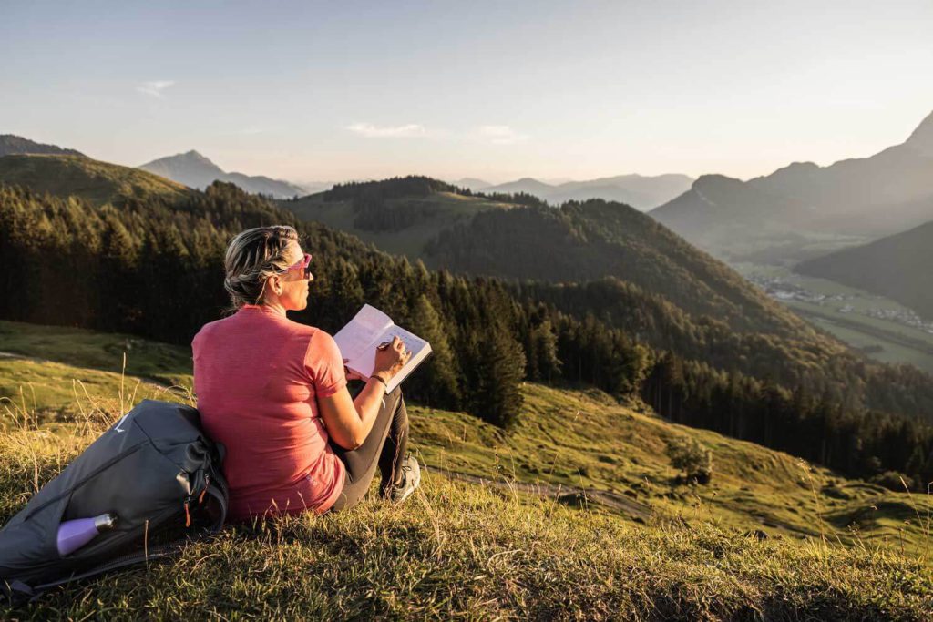Woman sits in the Tyrolean Alps and writes notes, surrounded by picturesque nature.