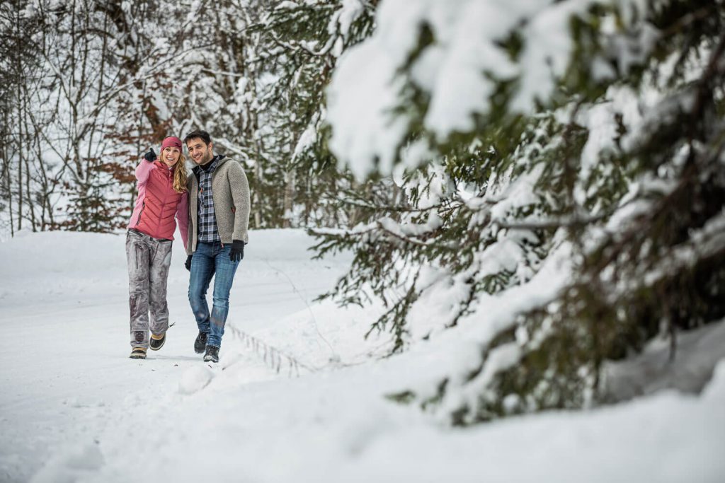 Winterliches Paar in Tirol, lachend bei einem Spaziergang im verschneiten Wald.