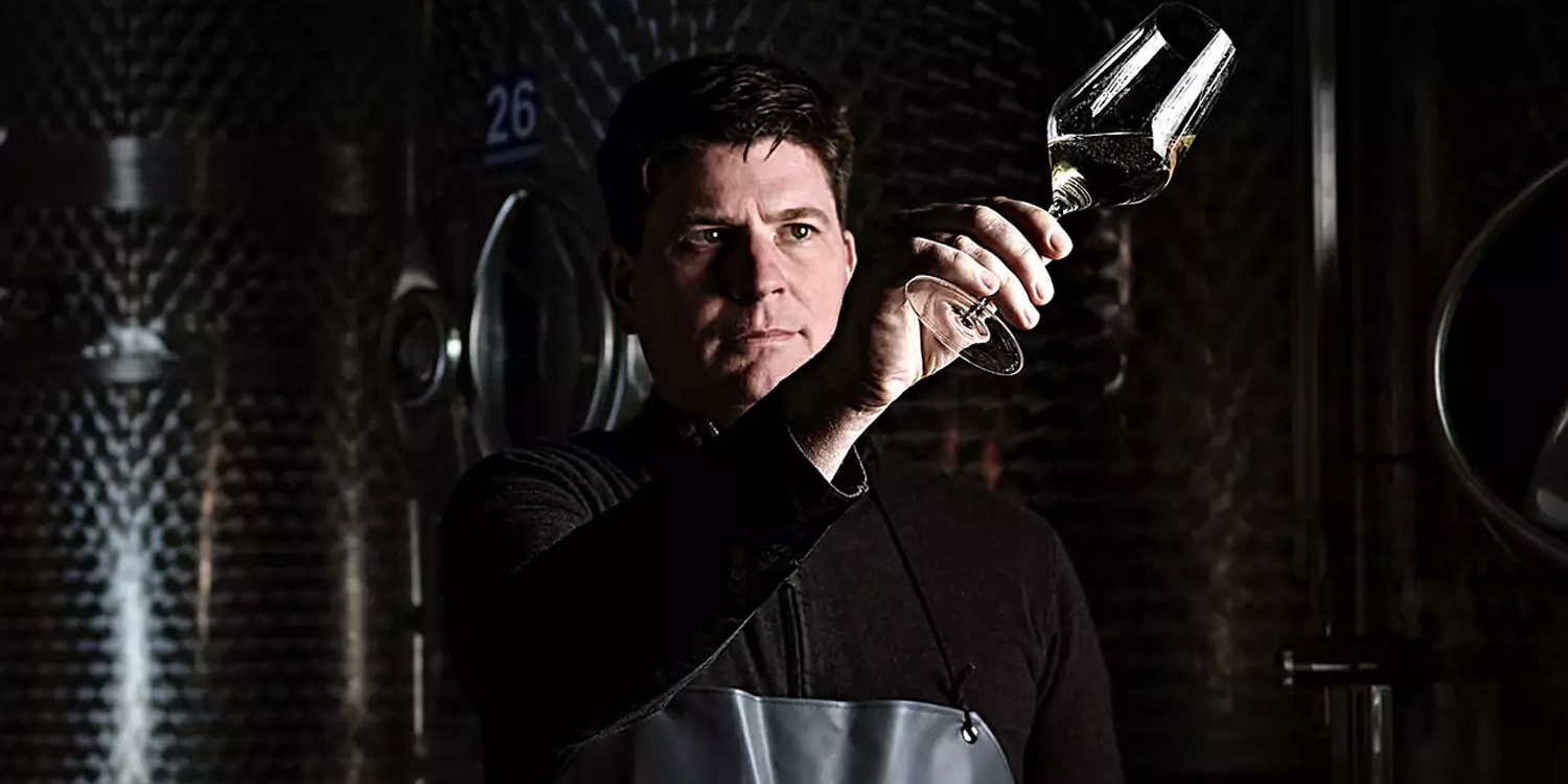 Eckhof Winery inspecting a glass of white wine in a wine cellar in front of stainless steel tanks