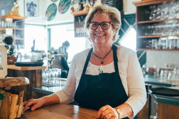 Donna sorridente in abito tradizionale dietro il bancone all'Hotel Penzinghof, Tirolo.