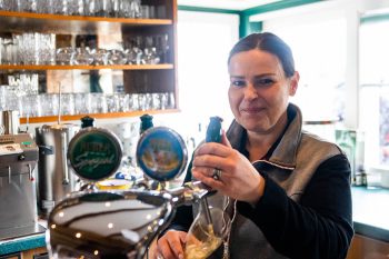 Una cameriera serve una bevanda al bar dell'Hotel Penzinghof, circondata da vetreria.