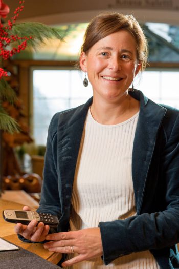 Addetta sorridente dell'Hotel Penzinghof con il telefono in mano, in un ambiente accogliente.