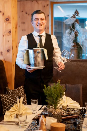 Addetto al servizio nell'elegante ristorante con secchiello per lo spumante e bicchieri, tavolo imbandito a festa.