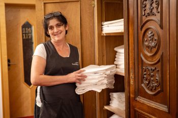 Addetta dell'Hotel Penzinghof con asciugamani freschi davanti a un armadio in legno.